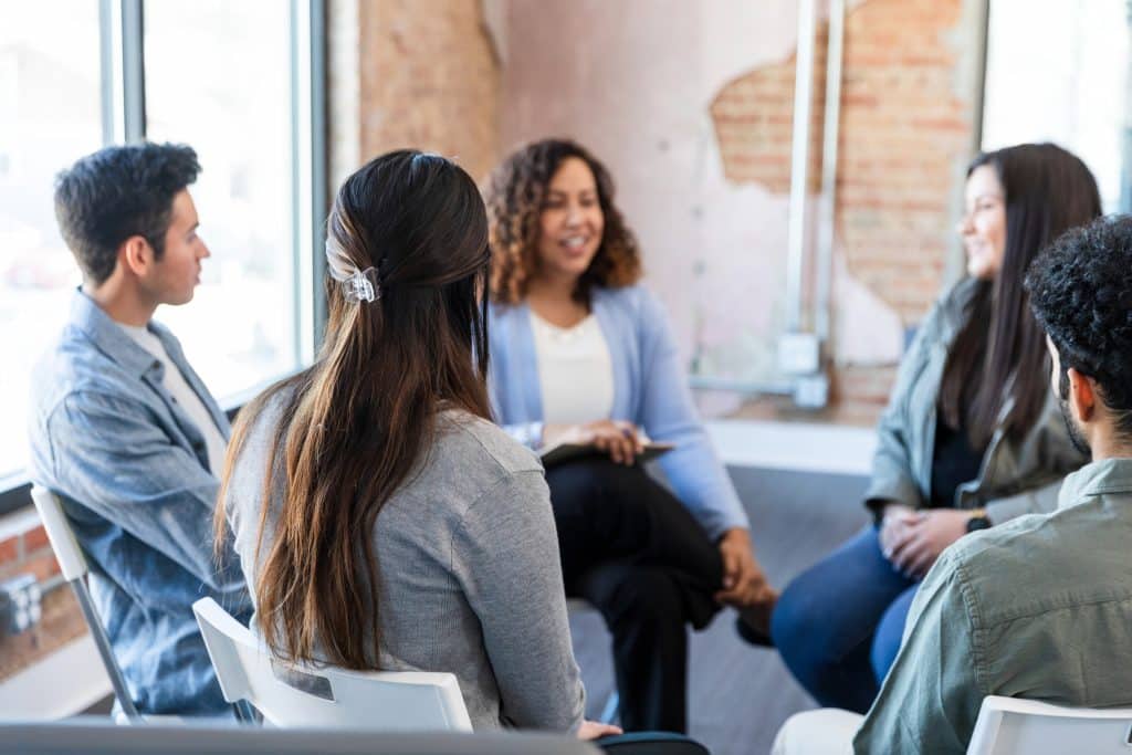 Small diverse group therapy session; adults talking and listening; emotional support and mental health.